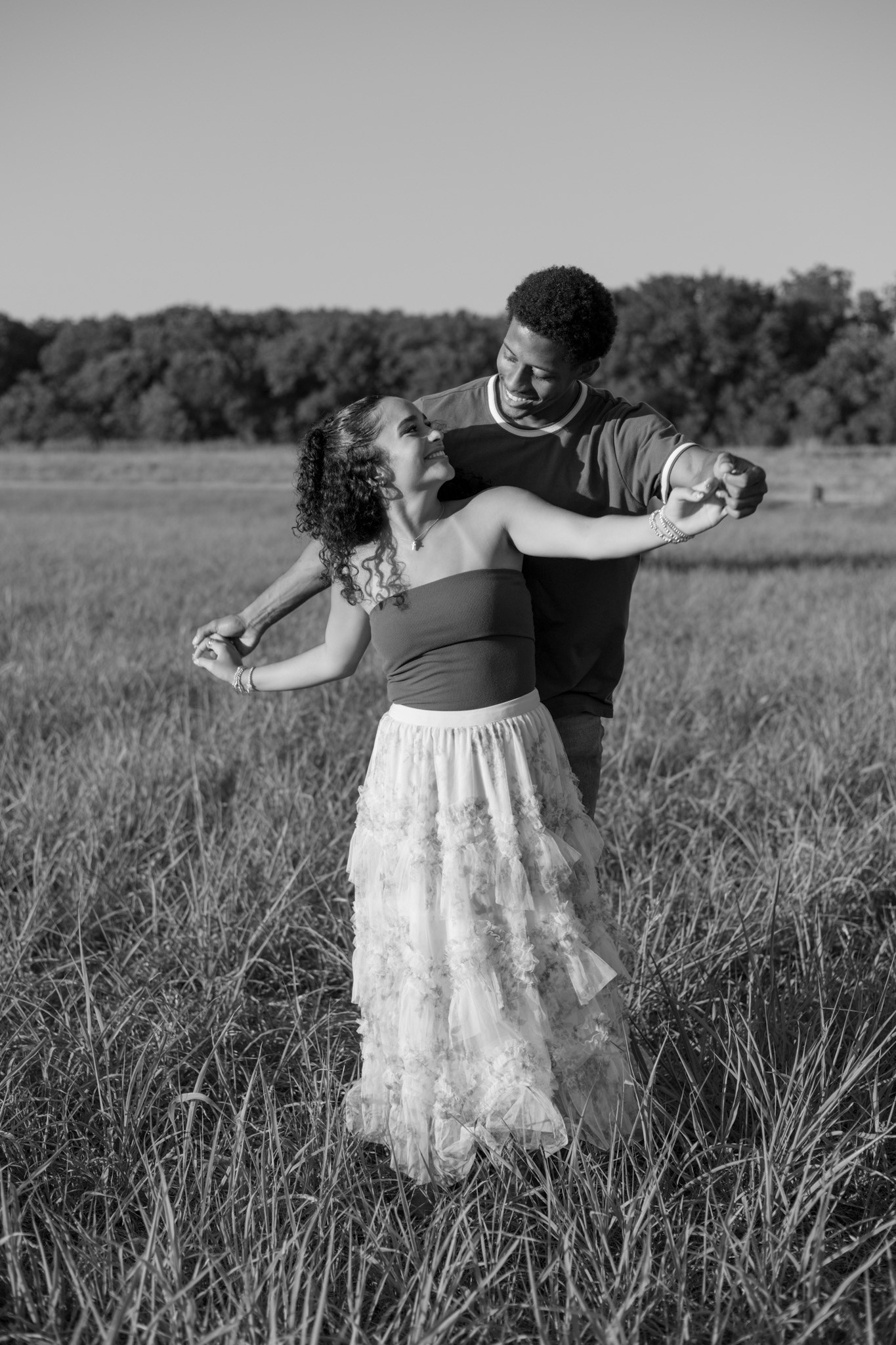 A black and white photo of a couple dancing in a field, the woman in a lace dress.