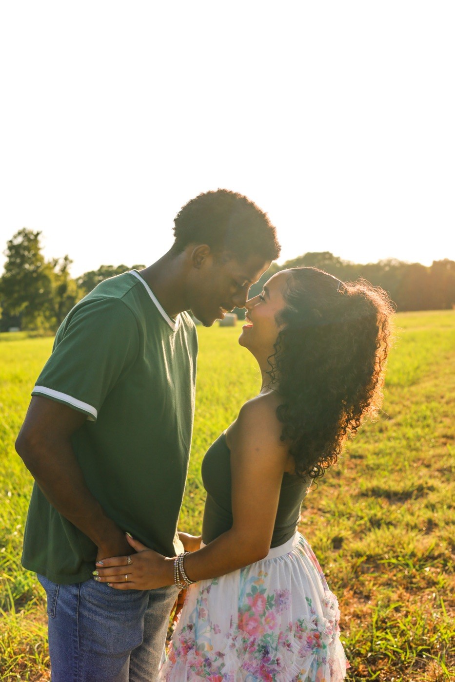A couple standing forehead to forehead in tall grass, backlit by low evening sun.