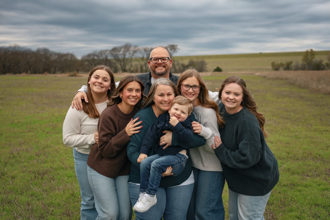 A family of seven gathered close together in an open North Texas field under a soft grey sky.