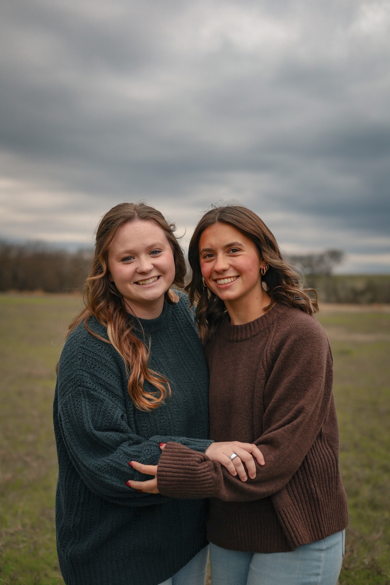 Two friends embracing in sweaters under an overcast sky.