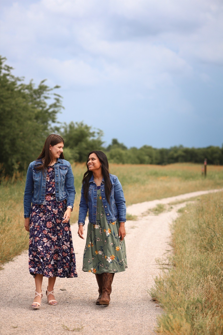 Two friends in floral dresses walking down a gravel path.
