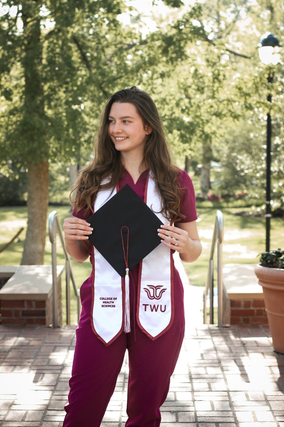 A Texas Woman&rsquo;s University graduate holding her cap and wearing her stole on campus.