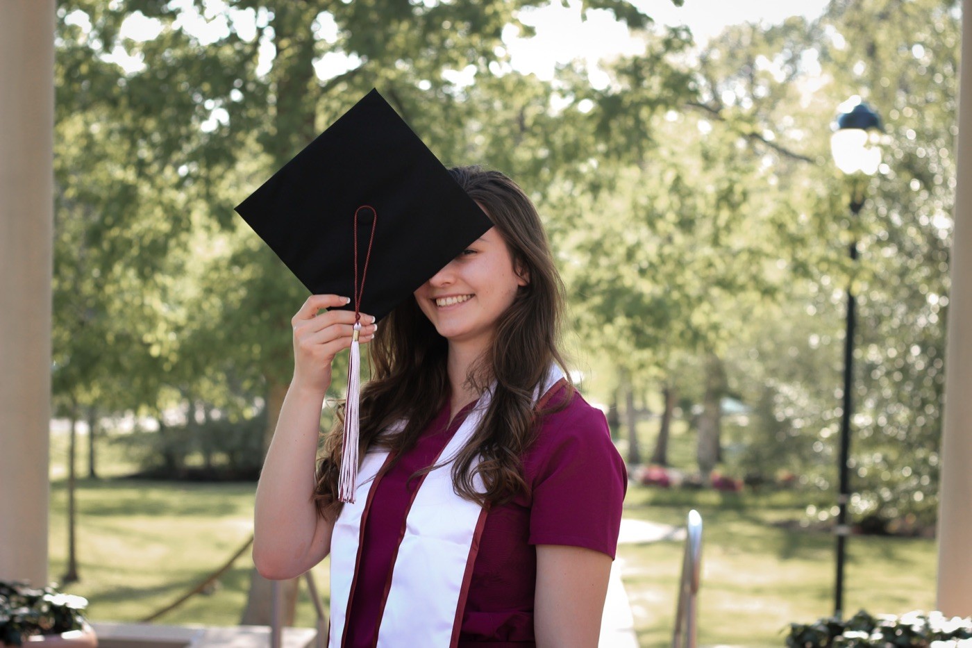 A graduate holding her cap over her face on a brick campus path.