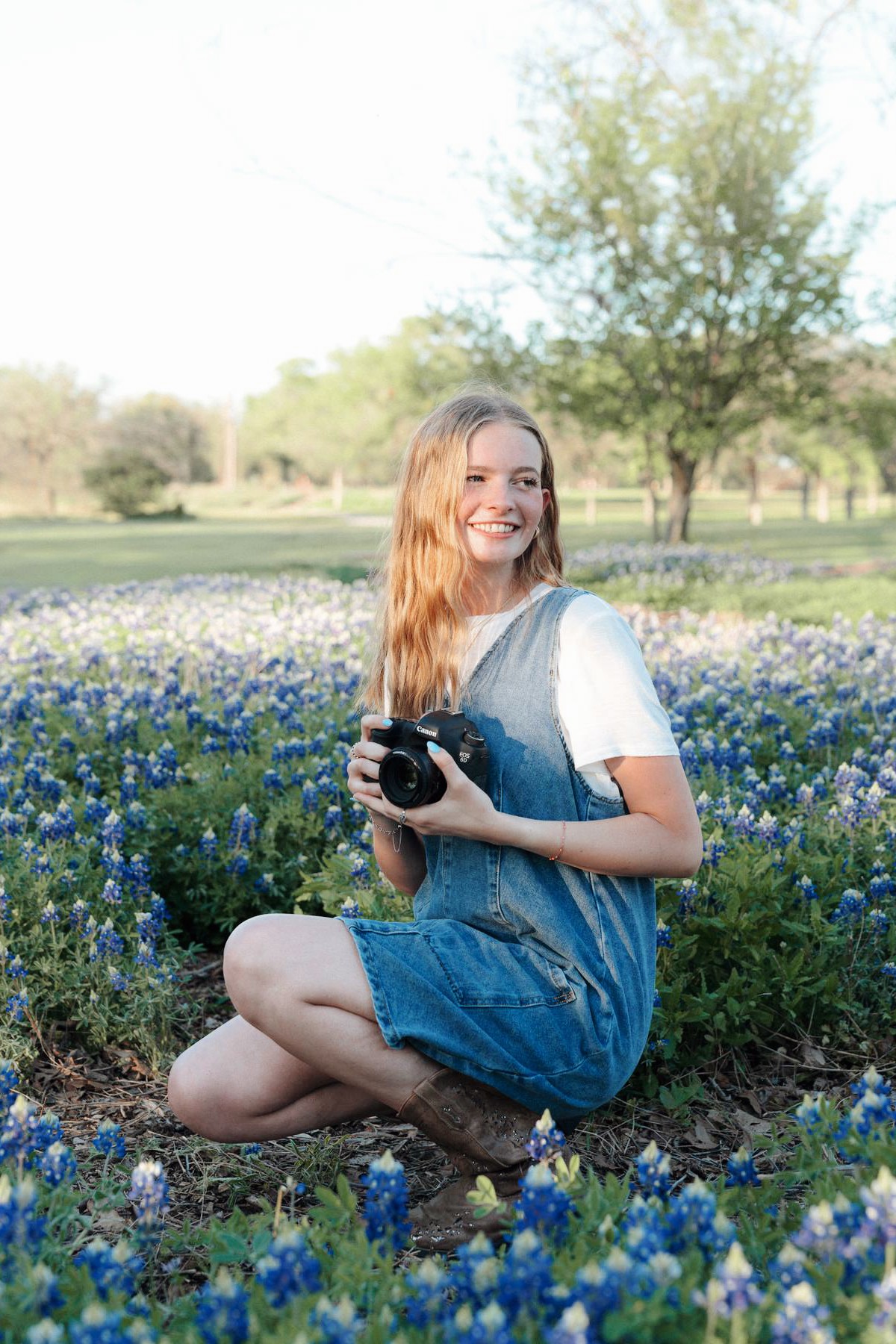 Piper, camera in hand, kneeling in a field of Texas bluebonnets.