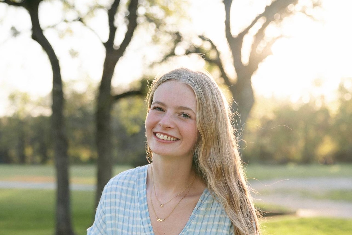 Piper smiling outdoors in a park at golden hour.