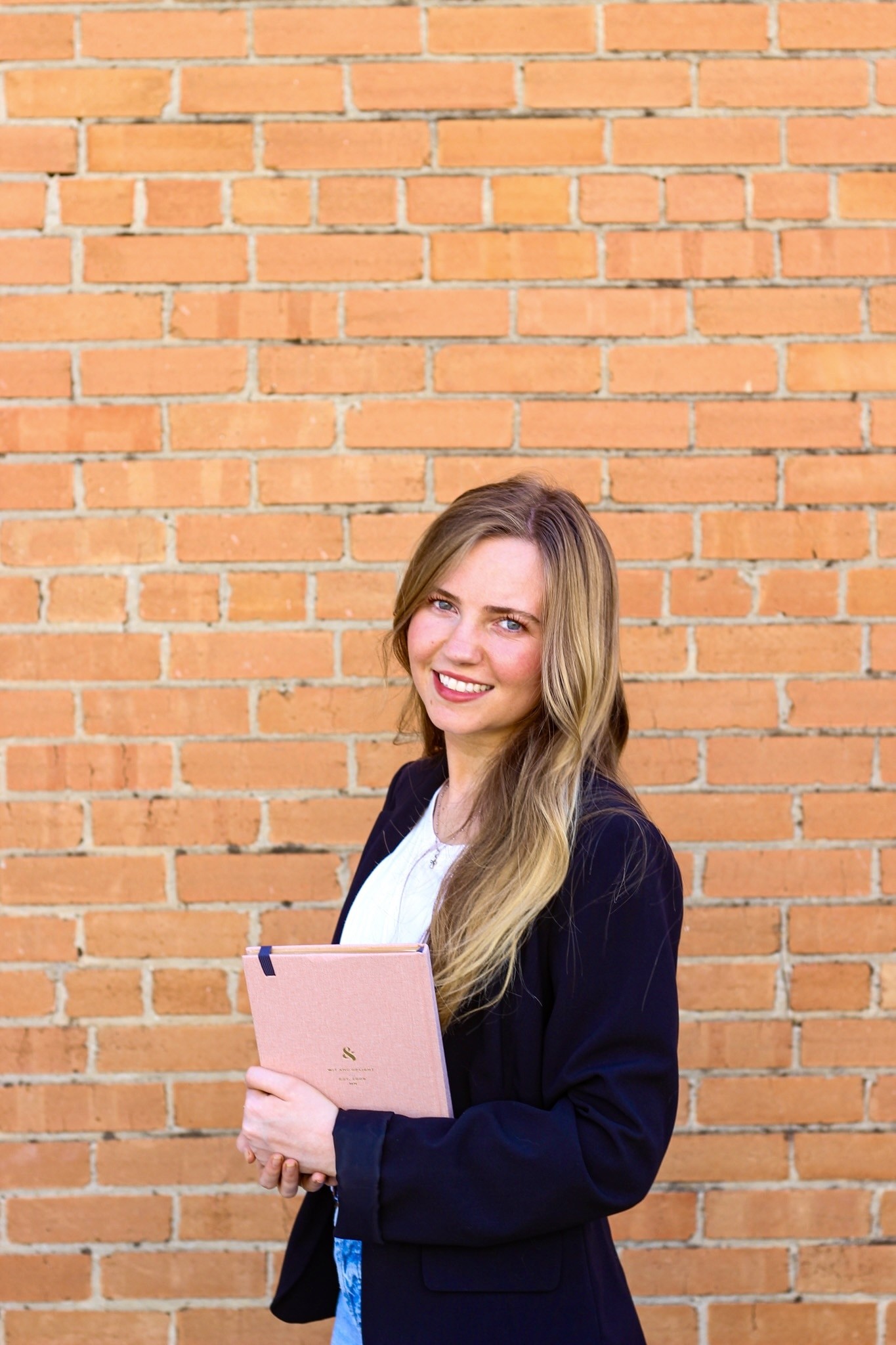A woman in a cardigan holding a tablet against a brick wall.
