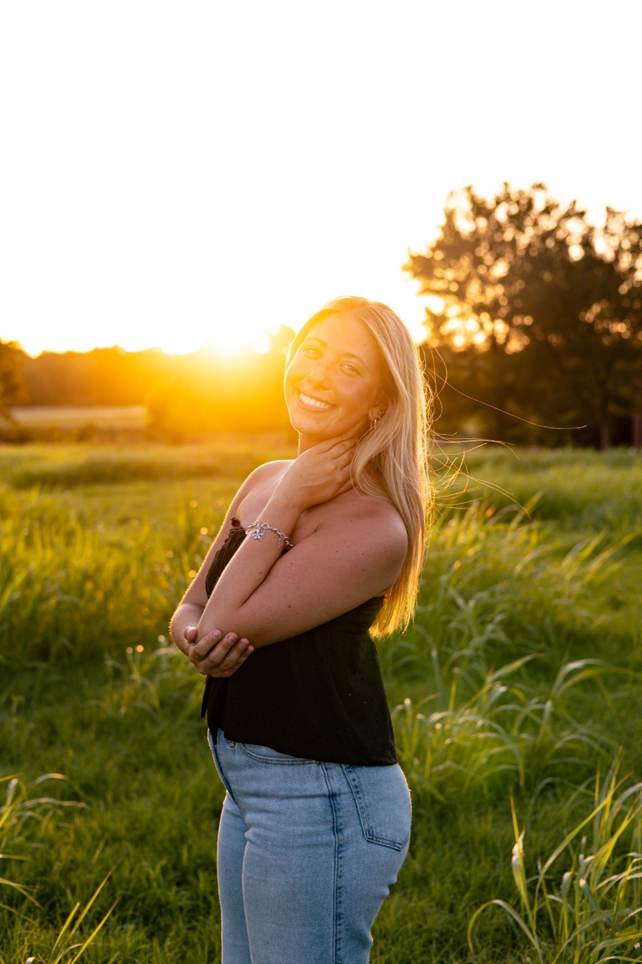 A senior laughing with her hand at her neck, backlit by golden hour sun.