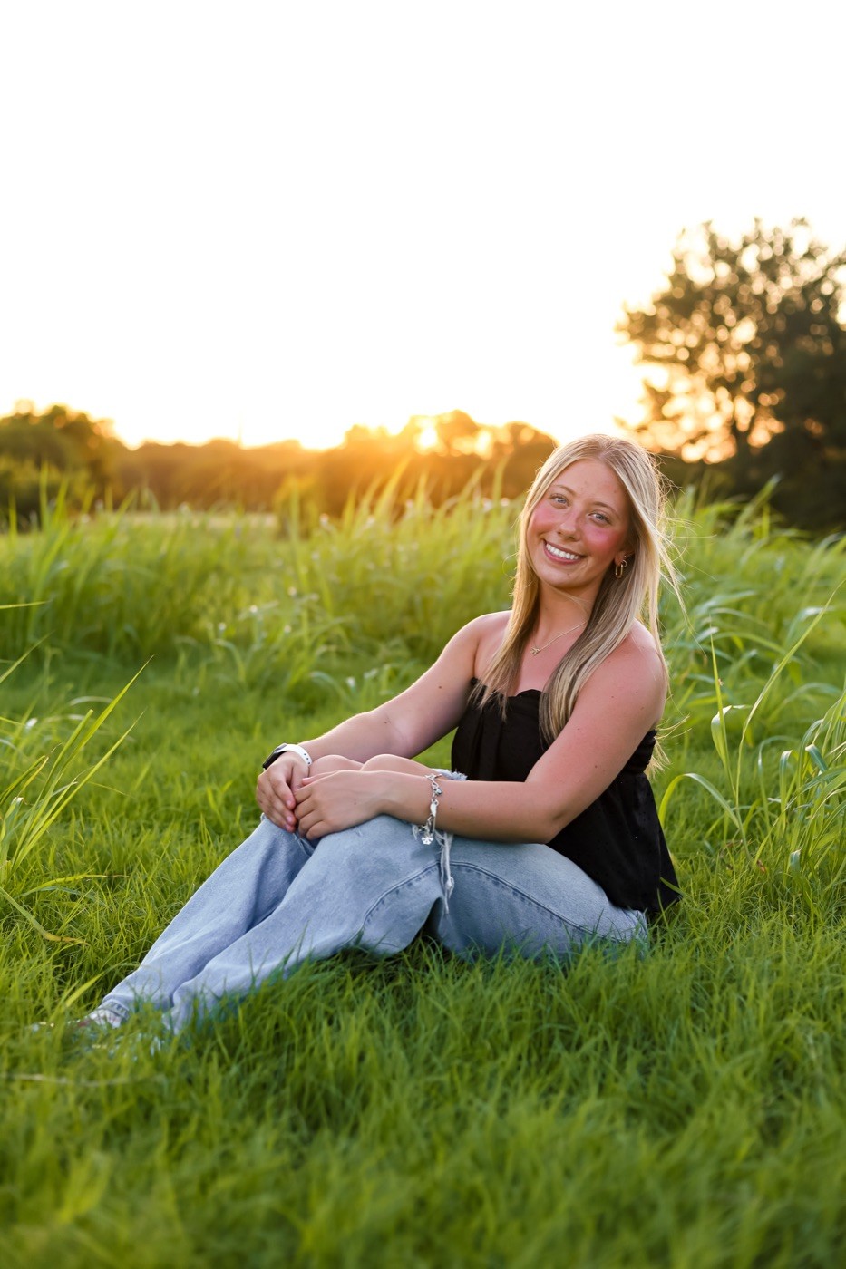 A senior sitting in tall grass at sunset.