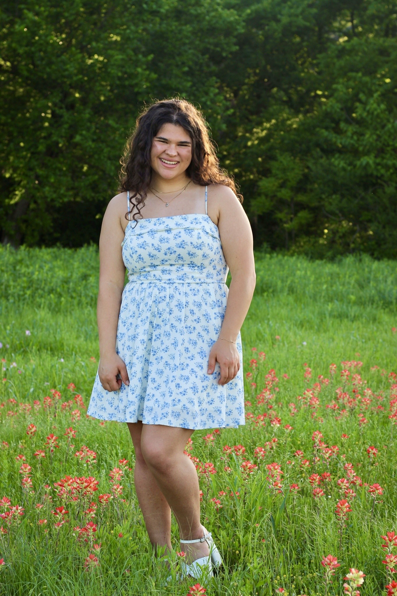 A senior in a blue floral dress standing among wildflowers.