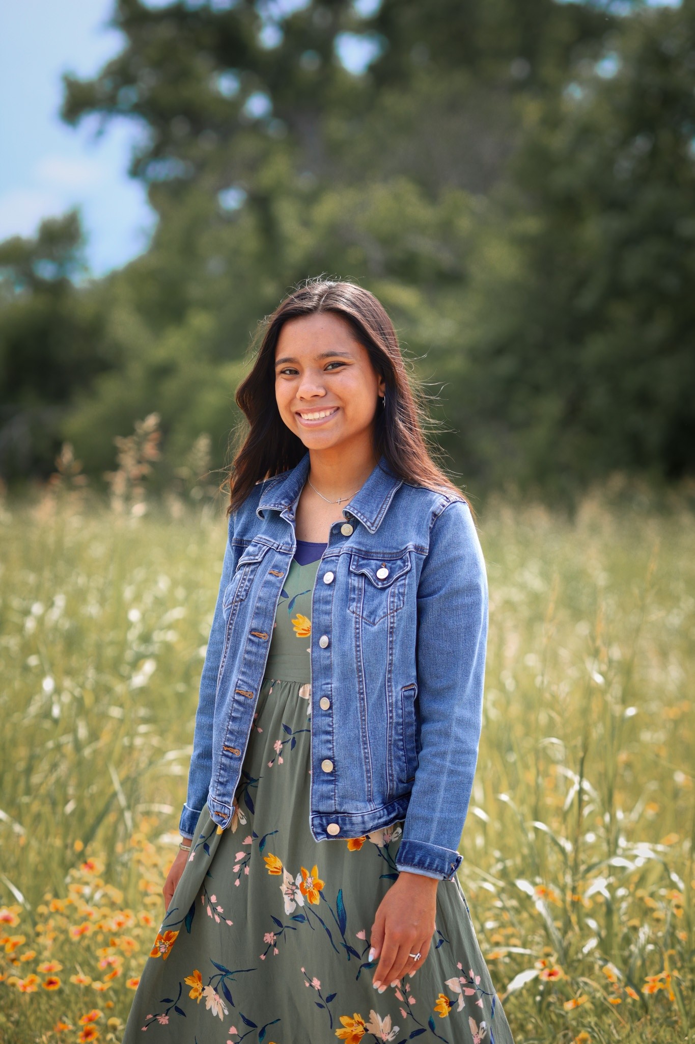 A senior in a green floral dress standing among wildflowers.